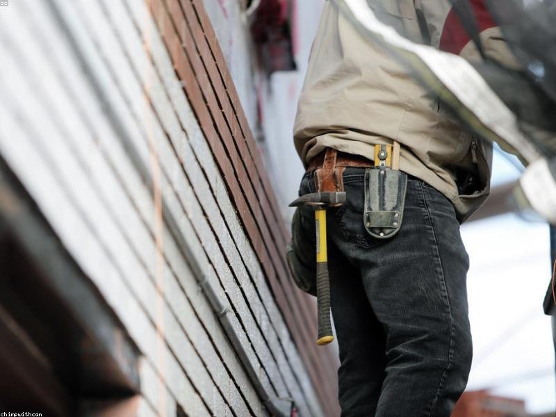 Contractor on a residential job site in tool belt, working on exterior brick and siding detail