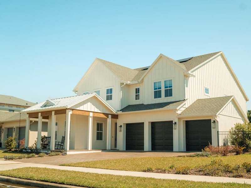 Newly built two-storey modern farmhouse with white board-and-batten siding, gabled roofs and triple garage — a finished custom home build